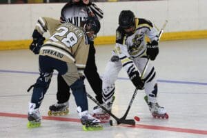 Two inline hockey players face off, competing for the puck on the rink with a referee observing.