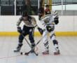 Two roller hockey players compete intensely on the rink, focused on the puck.