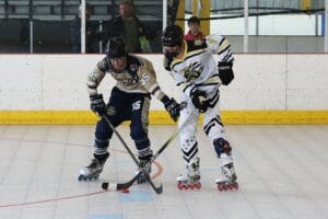 Two roller hockey players compete intensely on the rink, focused on the puck.