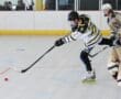 Roller hockey player shooting puck in indoor rink, wearing black and yellow gear.