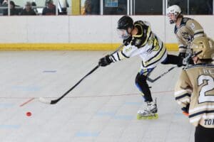 Roller hockey player shooting puck in indoor rink, wearing black and yellow gear.