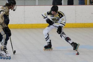 Two roller hockey players in action on the rink, one in white and yellow, challenging the other in beige.
