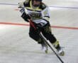Roller hockey player in action, wearing a white and black jersey, dribbling puck on rink.