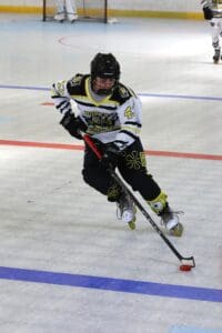 Roller hockey player in action, wearing a white and black jersey, dribbling puck on rink.
