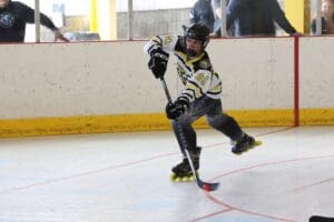 Roller hockey player in action, taking a dynamic shot on goal inside an indoor rink.