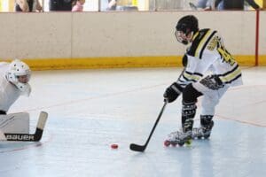Roller hockey player attempts a shot past goalie on indoor rink. Action-packed sports moment.