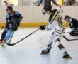 Roller hockey players in action on an indoor rink, wearing protective gear and colorful uniforms.