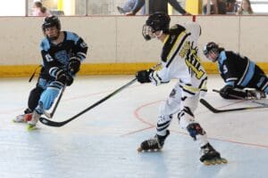Roller hockey players in action on an indoor rink, wearing protective gear and colorful uniforms.