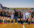 North Allegheny field hockey team poses on the field with their coach, holding posters of teammates in black uniforms.