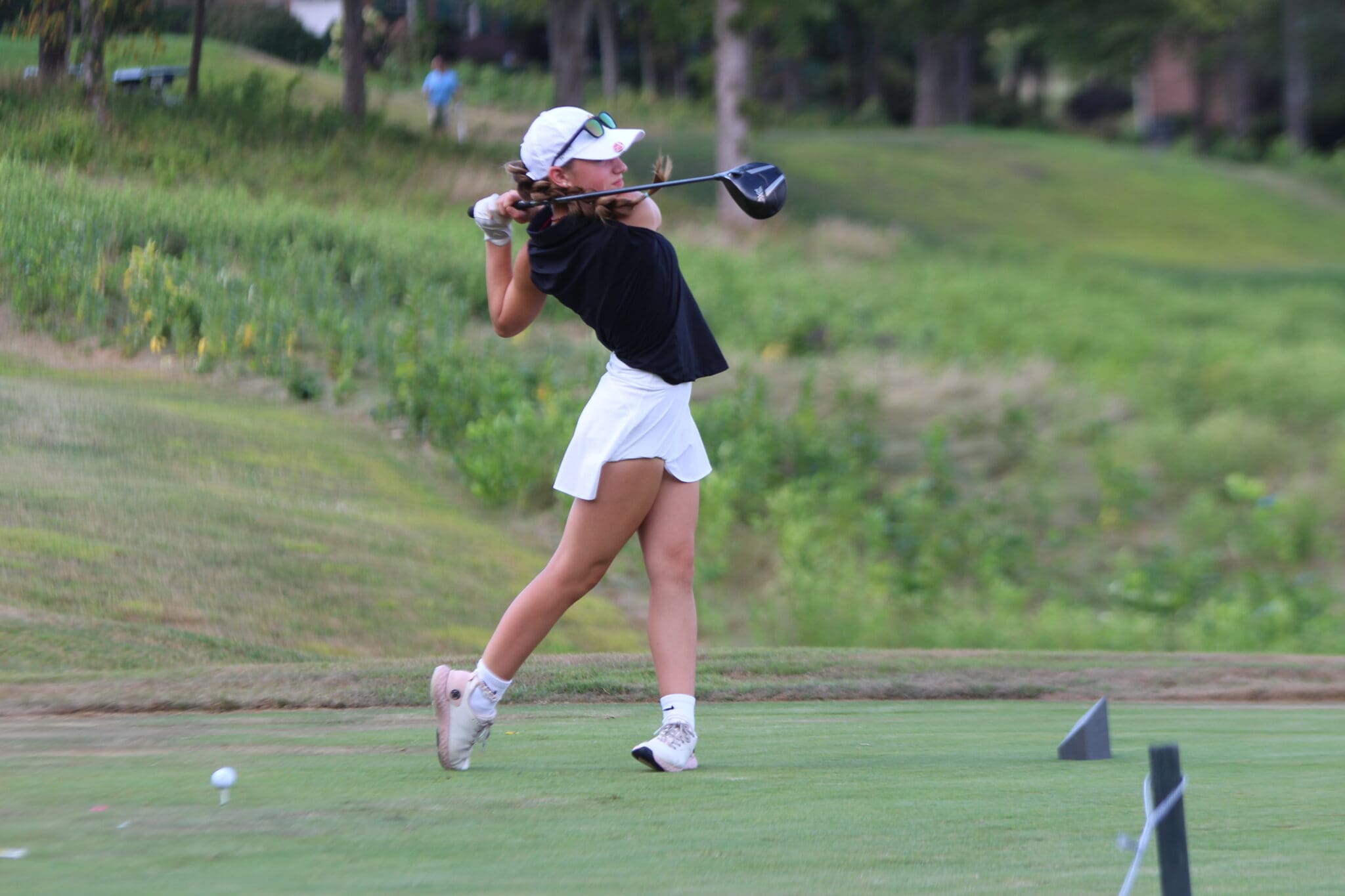 Young golfer swings club on lush green course, perfecting her technique.