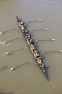 Eight-person rowing team moving synchronously on a river, showcasing teamwork and coordination in competitive rowing.