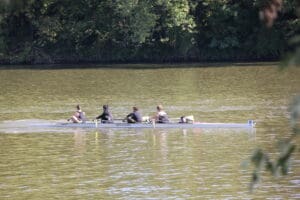 Rowing team practicing on a tranquil lake with lush green trees in the background.