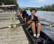 Rowing team prepares to launch from the dock under a blue sky, with one member giving a thumbs up.