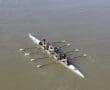 Four-person rowing team on a river, synchronizing strokes under clear skies.