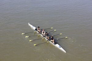 Four-person rowing team on a river, synchronizing strokes under clear skies.
