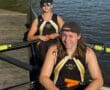 Two rowers in NA Crew jerseys sitting in a racing shell on the water, preparing for rowing practice.