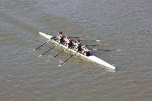 Four-person rowing team glides on water, displaying teamwork and synchronization in a sleek racing shell.