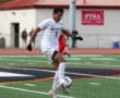 Soccer player in white jersey skillfully controls the ball mid-air on a green field during a match.