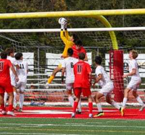 Soccer goalie jumps to catch the ball amid players in red and white uniforms during an intense match.
