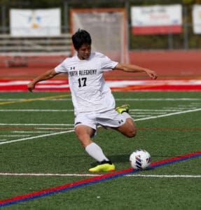 Soccer player in white jersey kicks a ball on a green field during a match.