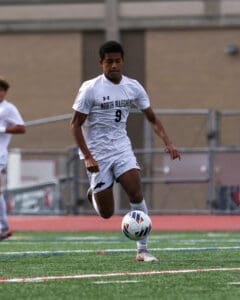Soccer player in white uniform controls the ball on a green field during a match.
