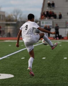 Soccer player in white jersey, number 9, mid-action on a field with blurred spectators in the background.