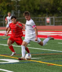 Two soccer players in action on the field, one in red and one in white, competing for the ball.