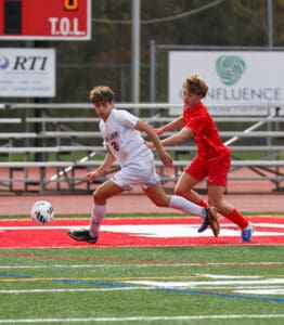 Two soccer players in action on a field, one in white and the other in red, competing for the ball.
