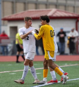 Two soccer players shake hands on the field after a match, showcasing sportsmanship and mutual respect.