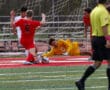 Soccer goalie in yellow saves goal as players in red and white compete on the field.