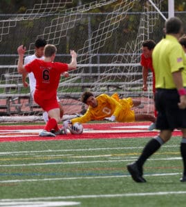 Soccer goalie in yellow saves goal as players in red and white compete on the field.