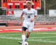 Soccer player dribbling ball on field with scoreboard in background during a match at Peters Township stadium.