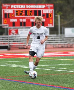 Soccer player dribbling ball on field with scoreboard in background during a match at Peters Township stadium.