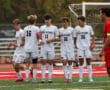 Soccer players in white uniforms preparing for a match on a green field.