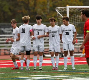 Soccer players in white uniforms preparing for a match on a green field.