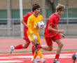 Soccer player in yellow and opponents in red on a field, mid-game action.