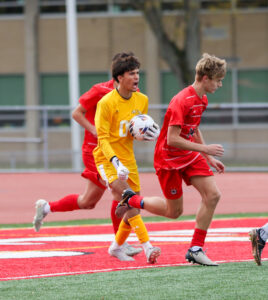 Soccer player in yellow and opponents in red on a field, mid-game action.