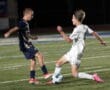 Two soccer players in action on the field, one in navy and the other in white, competing for the ball.