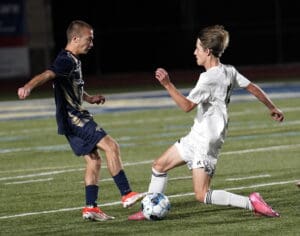 Two soccer players in action on the field, one in navy and the other in white, competing for the ball.