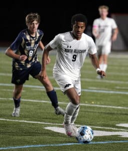 Soccer player dribbling the ball during a match between North Allegheny and Butler, wearing a white jersey with number 9.