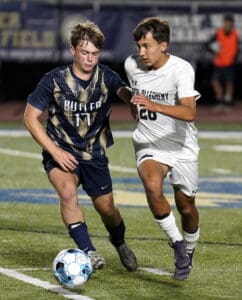 Two soccer players in action on the field during a night game, competing for the ball.