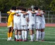 Soccer team in white jerseys huddling for a pre-game strategy on the field, fostering teamwork and unity.