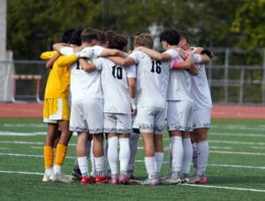 Soccer team in white jerseys huddling for a pre-game strategy on the field, fostering teamwork and unity.