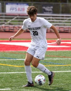 Soccer player in white uniform dribbling ball on field during daytime game.