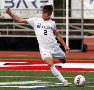 Soccer player in white kit striking ball on field during match, displaying athletic skills and focus.