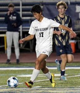 Soccer player in white uniform dribbles ball during a high school match, focused and in motion on the field.