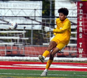 Soccer goalie in yellow kit kicks the ball mid-air during a match, sporting focused expression.
