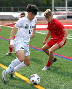 Young soccer players in action, one in white dribbling past the opponent in red on a green field.