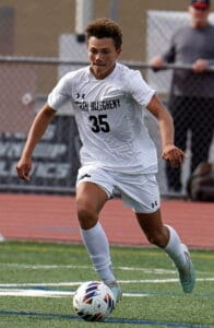 Soccer player in white uniform dribbling on a field during a game.