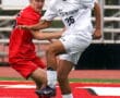 Two soccer players compete for the ball on a field, wearing red and white uniforms.